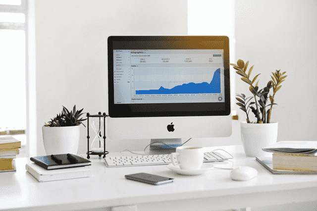 iMac desktop displaying a business analytics chart on a clean desk with a potted plant