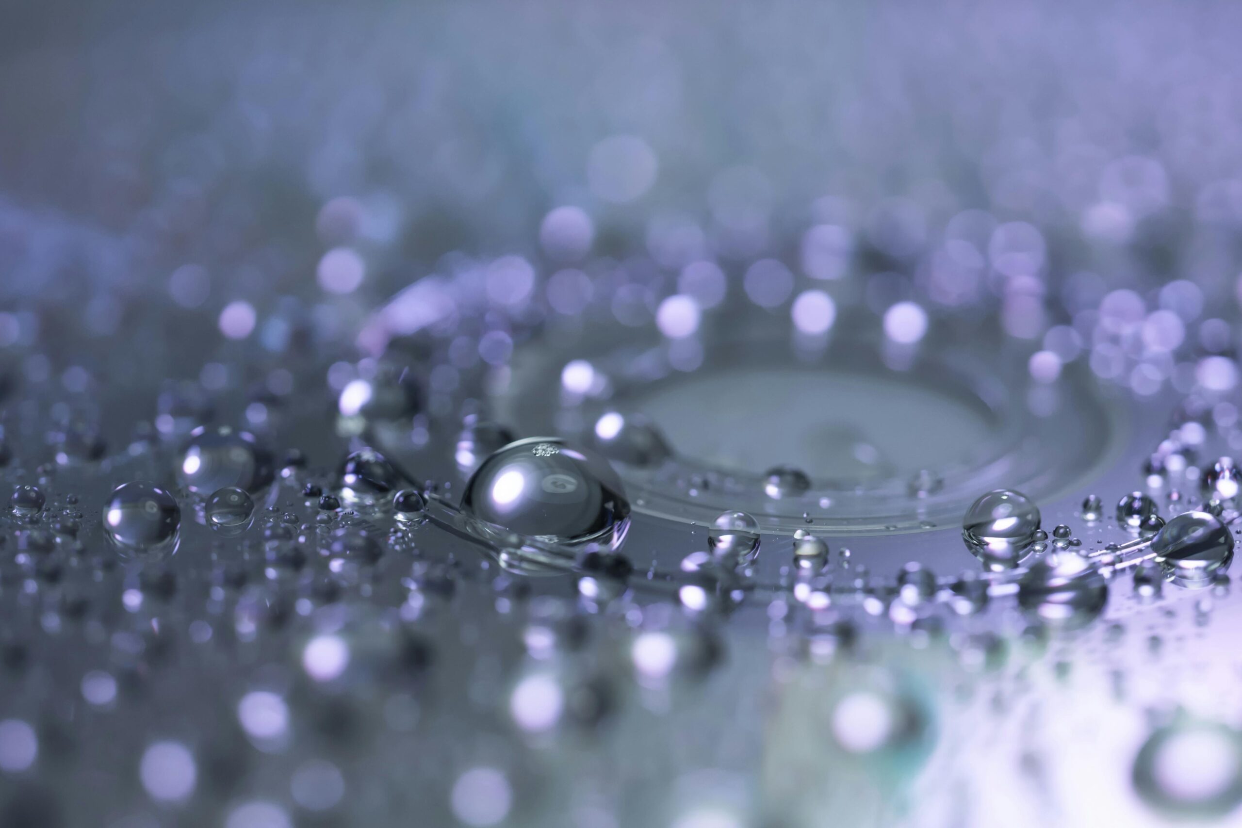 Macro close-up of clear water droplets on a dark surface with soft bokeh background
