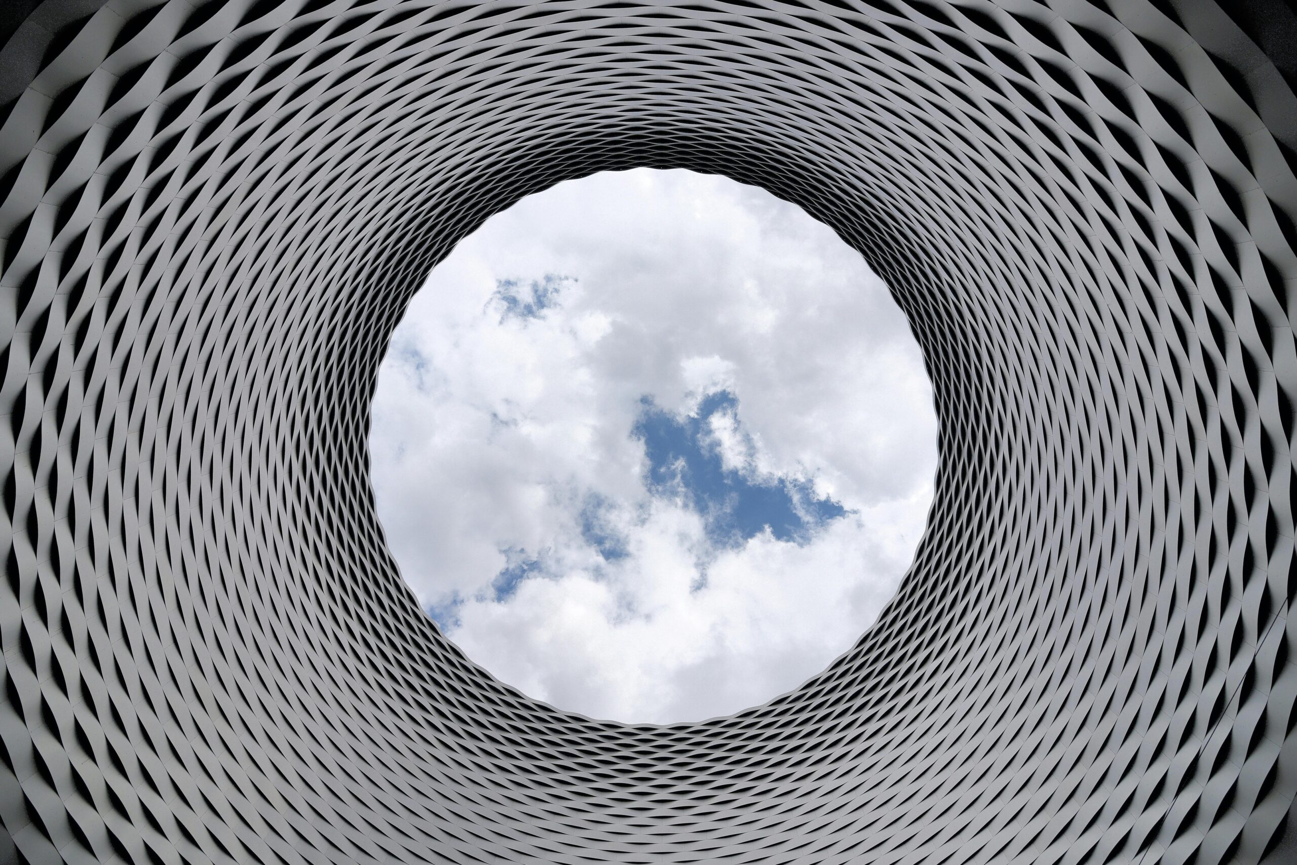 Looking up through a circular concrete architectural opening toward a cloudy sky
