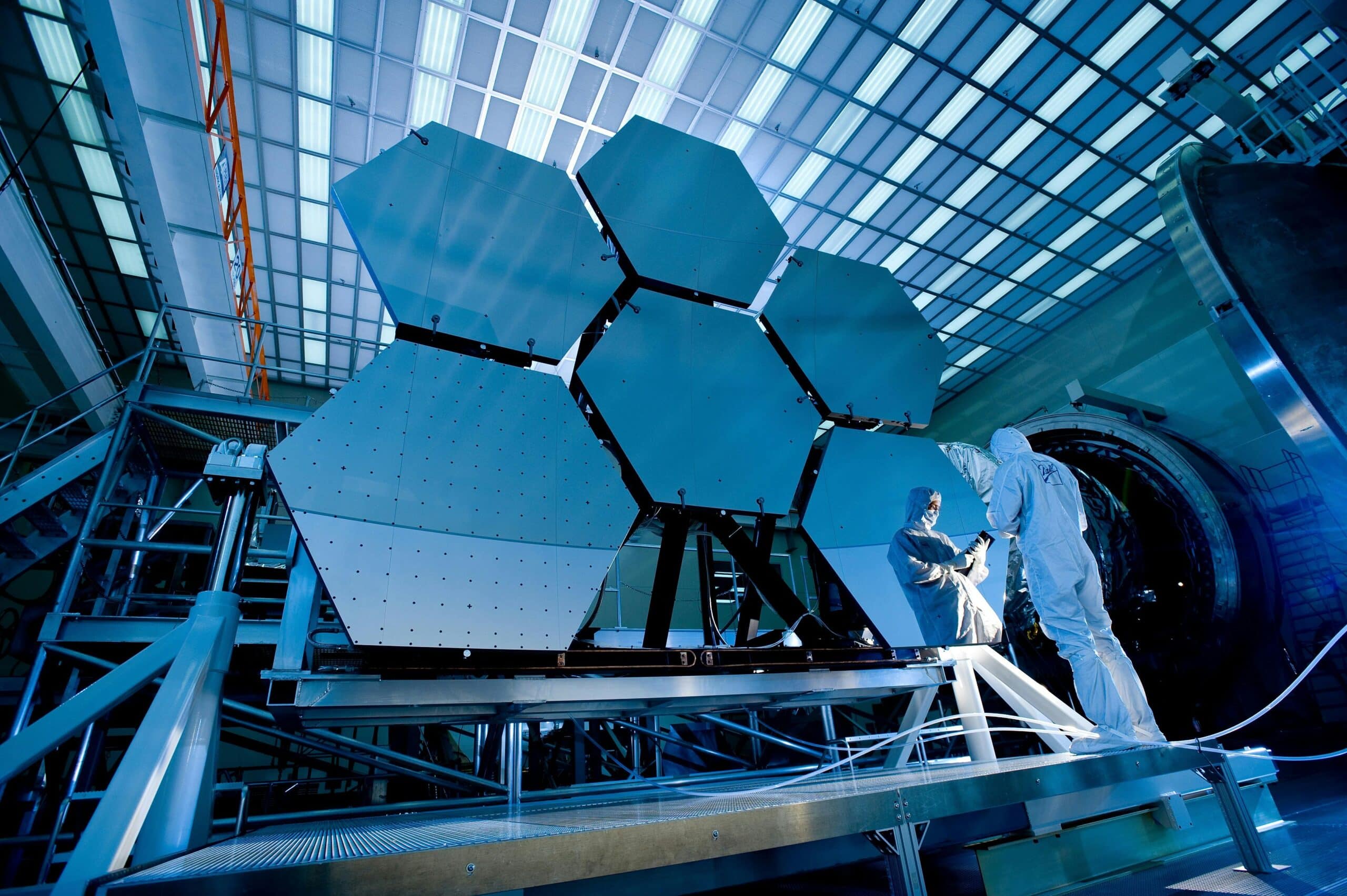 Engineering workers in hard hats assembling a large hexagonal telescope mirror array